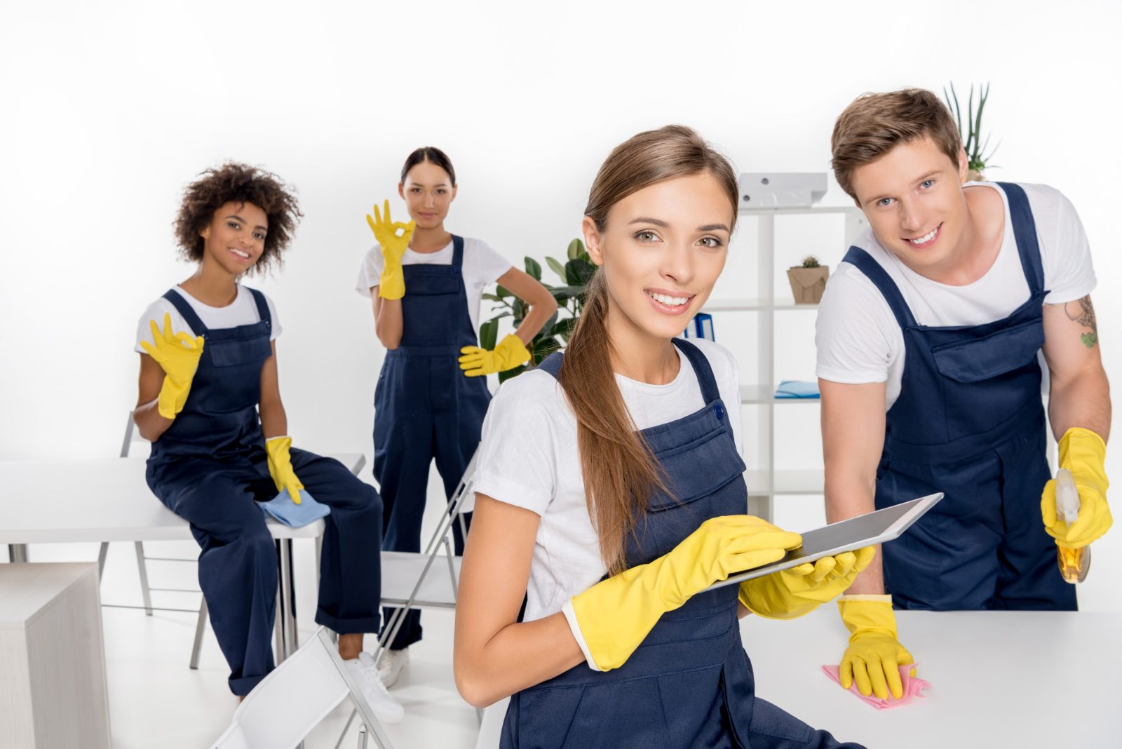 Group of six smiling cleaning staff in beige uniforms holding cleaning supplies in a bright living room.