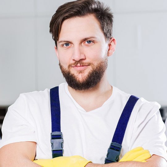 Smiling woman in cleaning uniform holding spray bottle and cloth in a bright, modern kitchen.