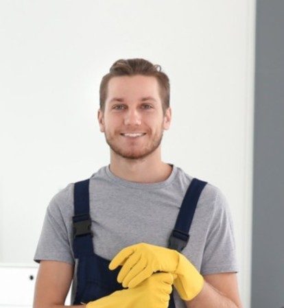 Smiling woman in beige cleaning uniform with a sparkling star icon, holding a mop and wearing yellow rubber gloves in a bright living room.